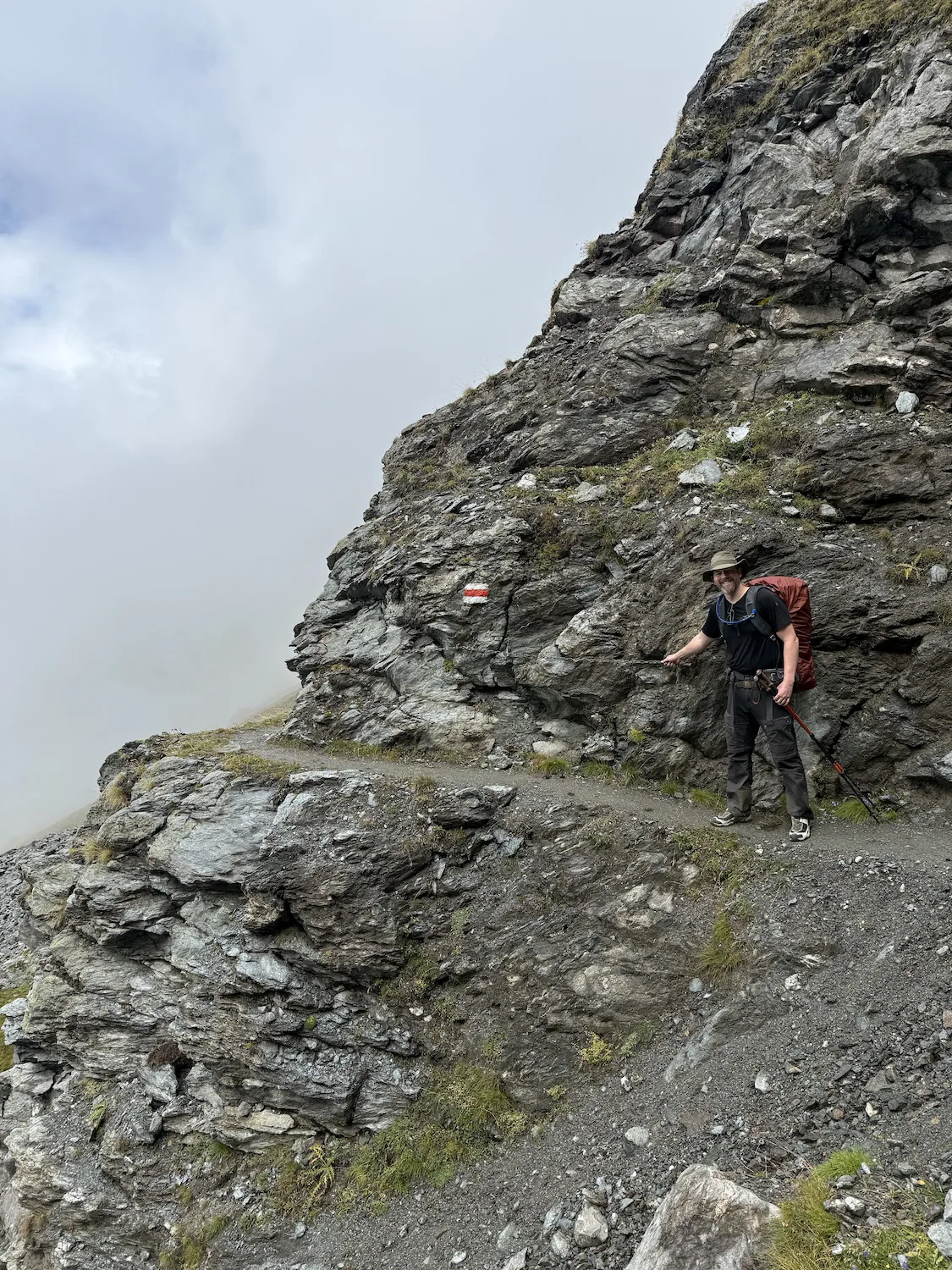 Man hiking using chain attached to mountain on a steep section